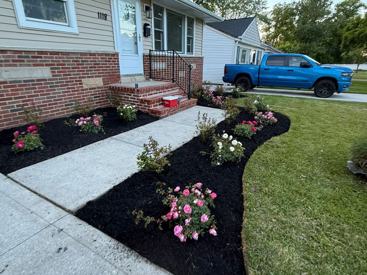 Cantero con mulch fresco y flores frente a una casa
